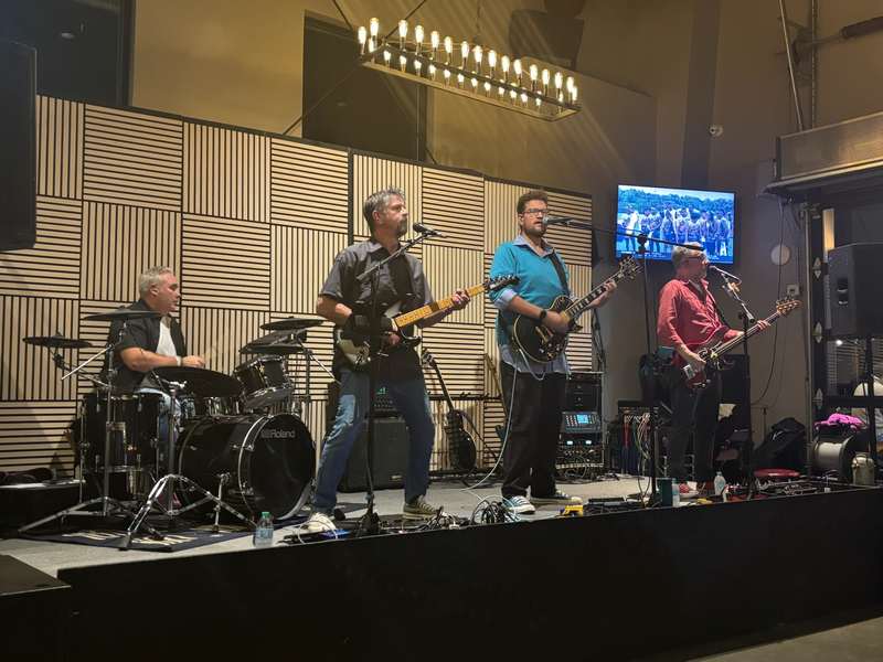 Tony and the full band performing on a modern indoor stage